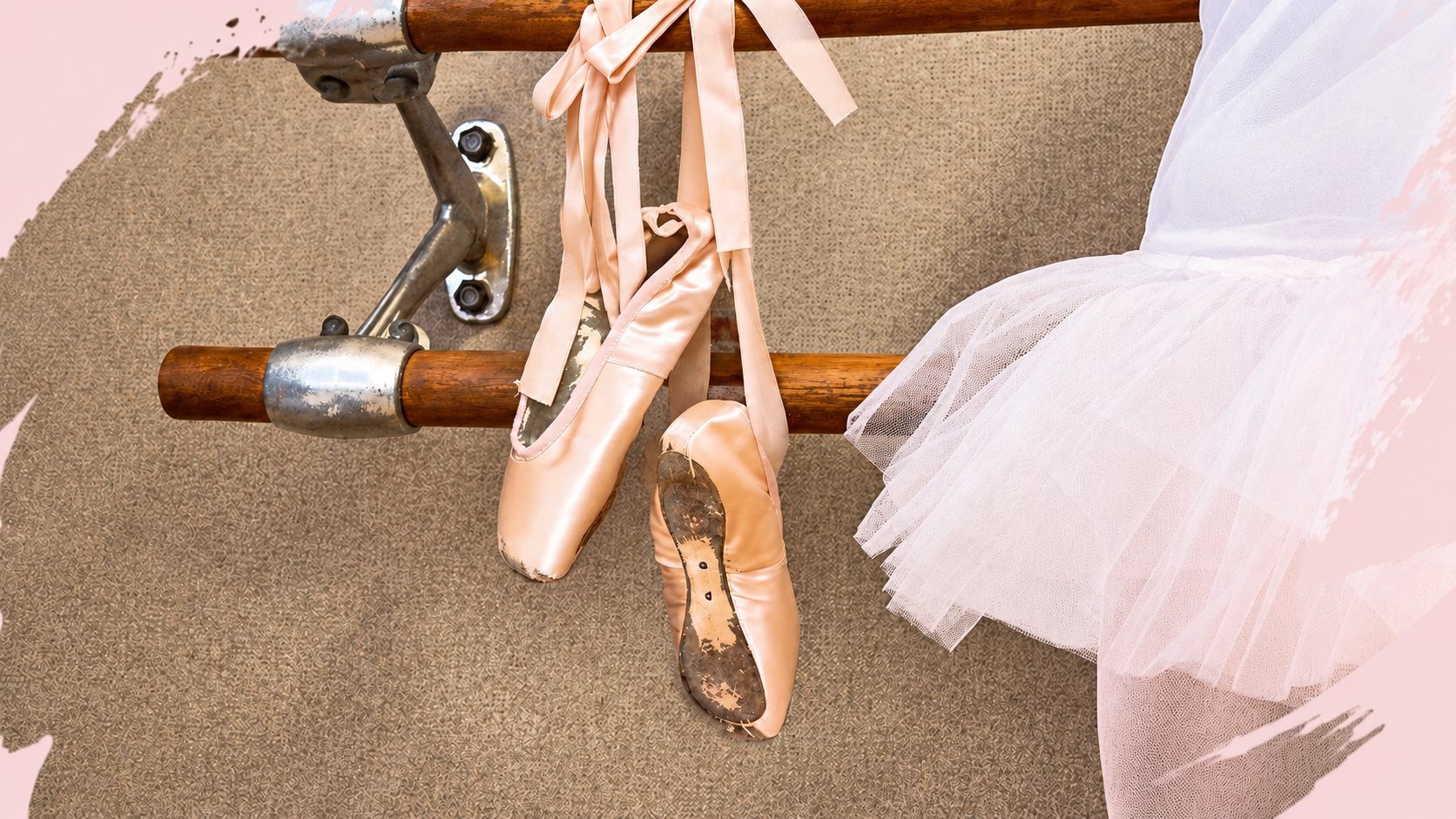 Une paire de chaussons de pointe roses est accrochée par ses rubans à une barre de danse en bois, à côté d'un tutu blanc.