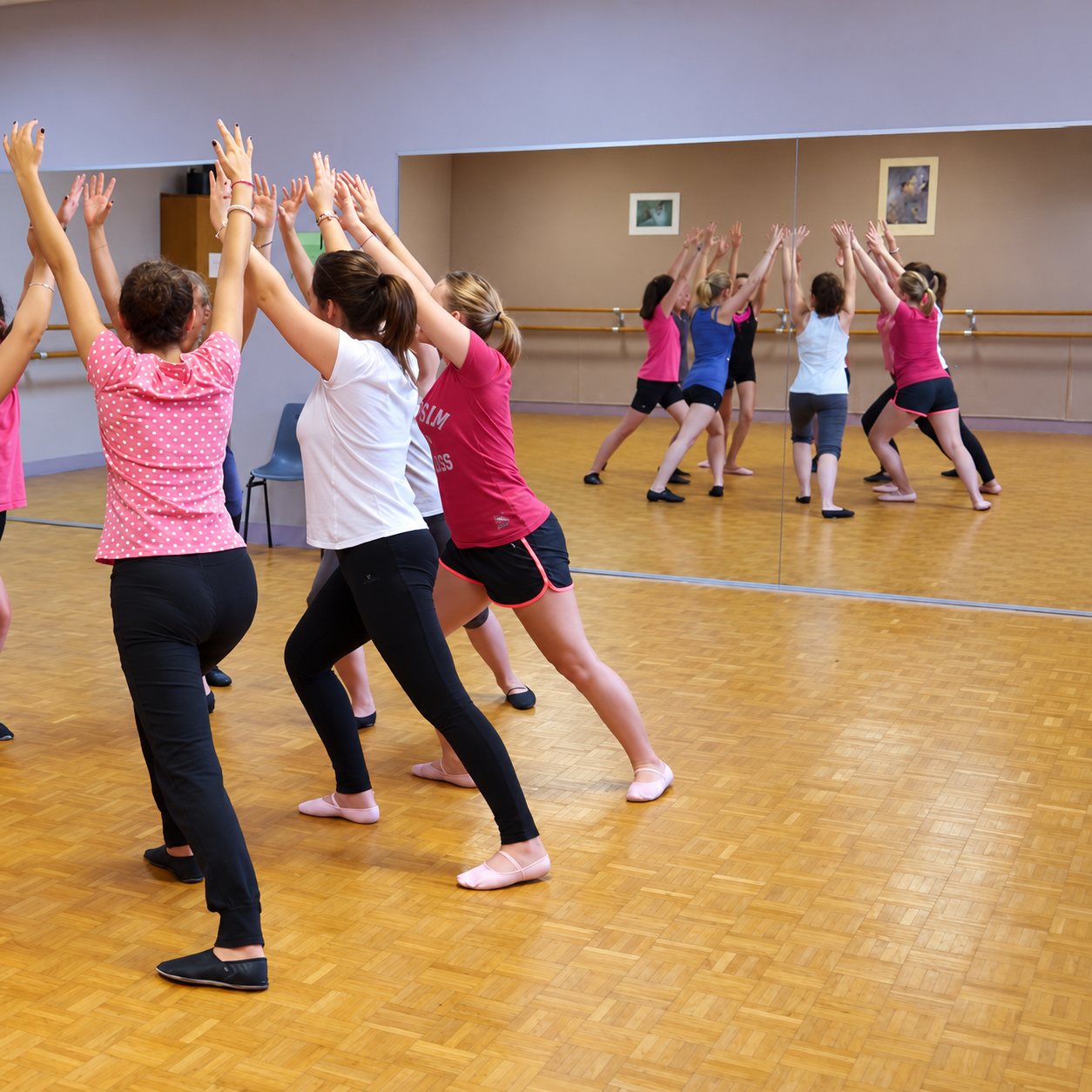 Un groupe de danseuses lève les bras en fente avant pendant un cours dans une salle avec miroir et parquet.