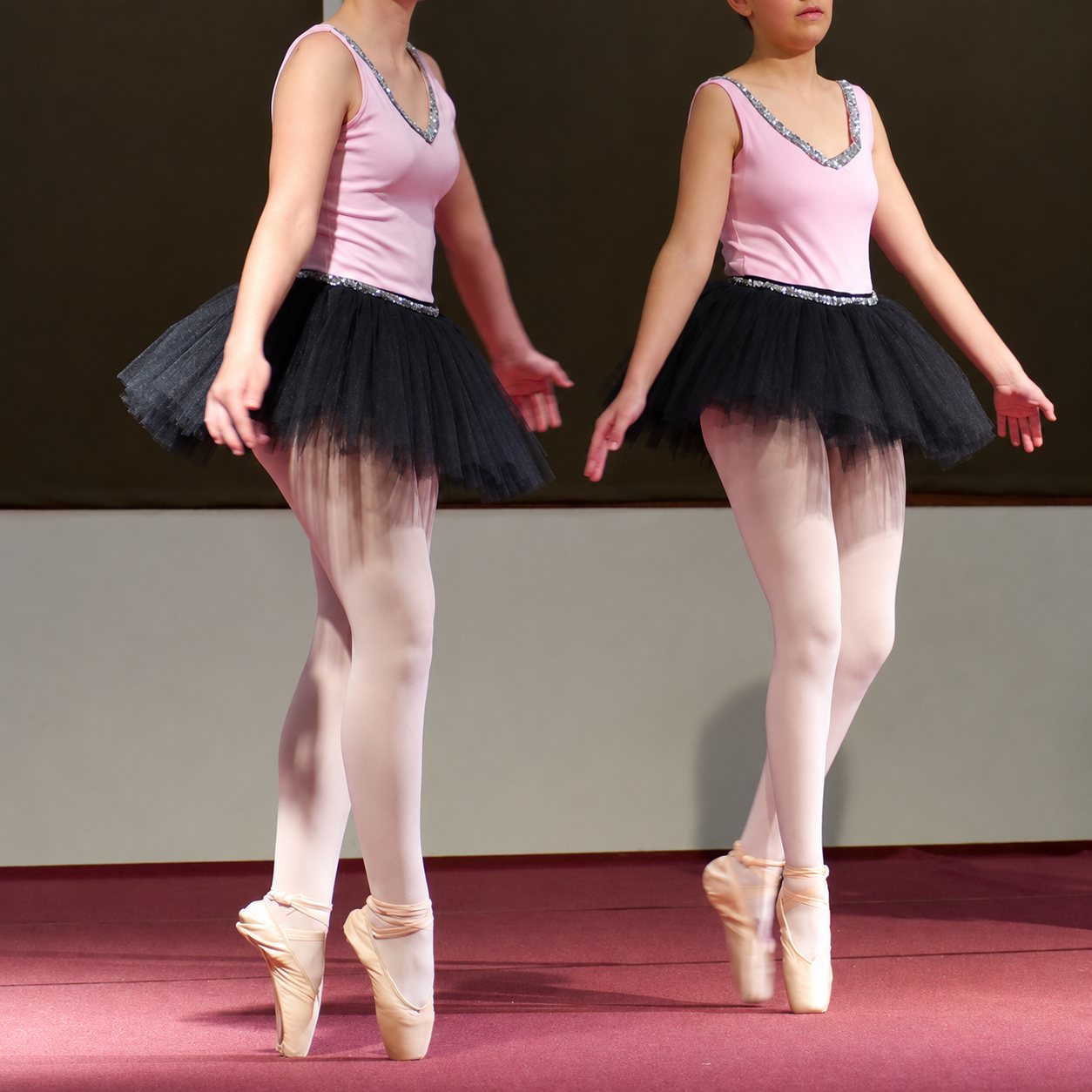 Deux danseuses classiques en justaucorps rose et tutu noir se tiennent sur les pointes lors d'un spectacle.