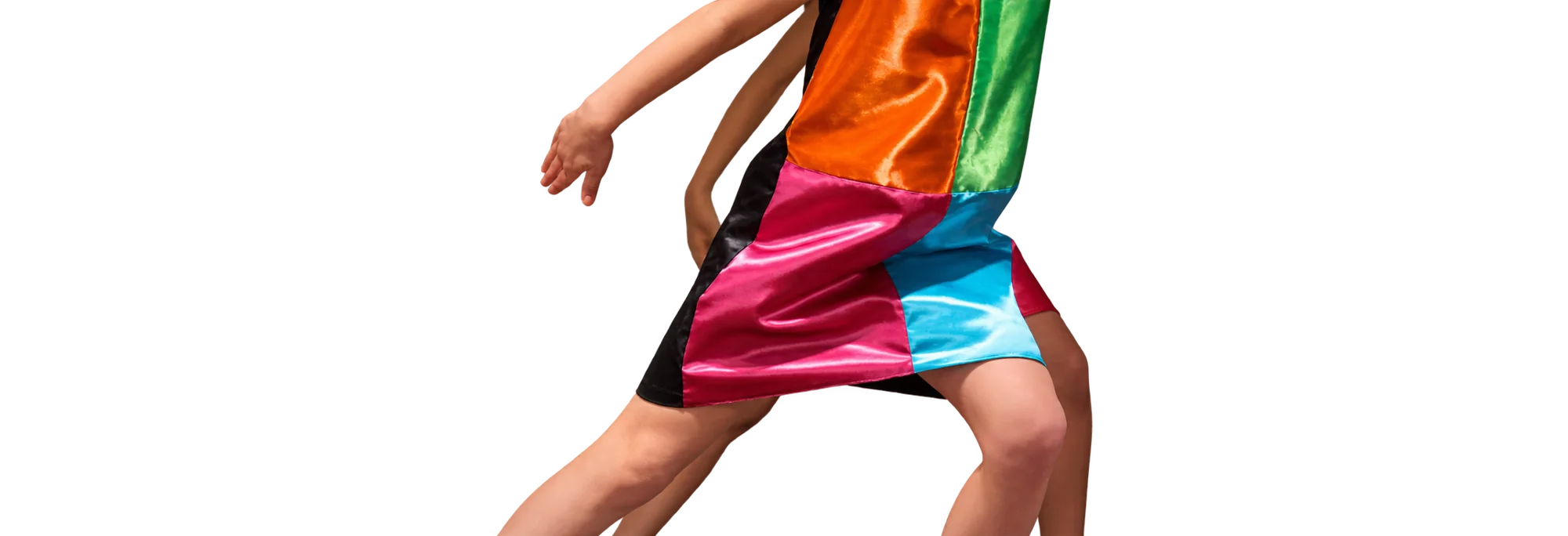 Une personne en mouvement, cadrée du torse aux genoux, porte une robe courte en satin composée de panneaux orange, vert, rose, bleu et noir devant un mur uni sombre.